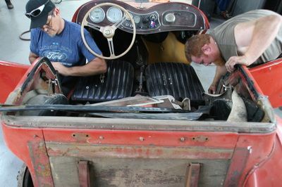 Two men are working on a red car in a garage
