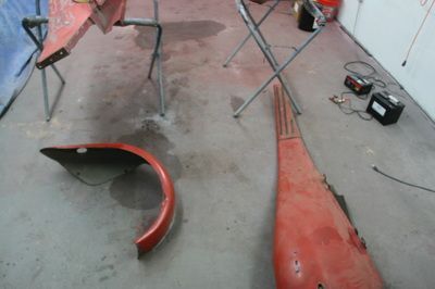 A red fender is laying on the floor in a garage