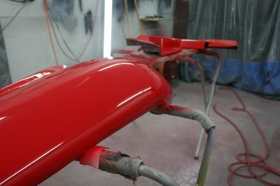 A red car is being painted in a garage