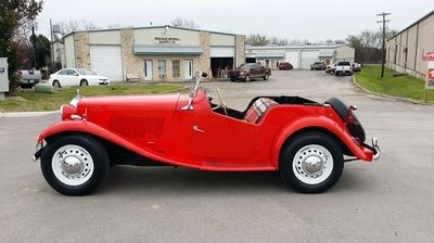 A red car is parked in a parking lot in front of a building