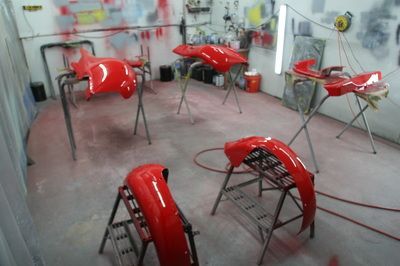 A bunch of red fenders are sitting in a paint booth