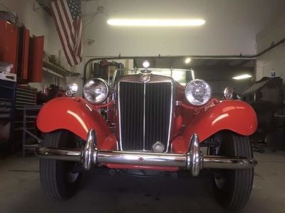 A red car is parked in a garage with an american flag hanging from the ceiling