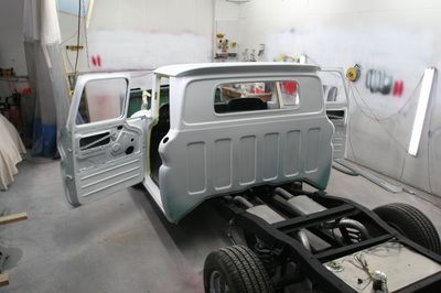A van is being painted in a garage with its doors open