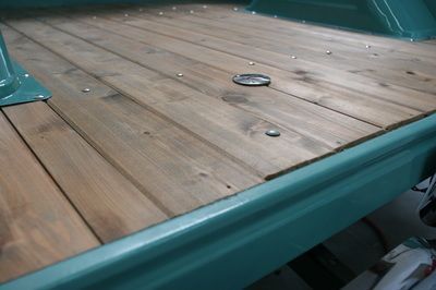 The back of a green truck with a wooden floor