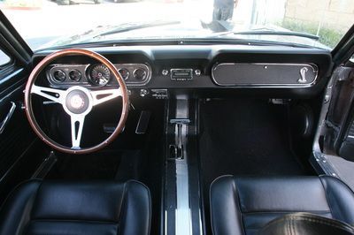 The interior of a ford mustang with black seats and a wooden steering wheel