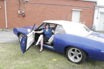 A woman is sitting in a blue car with her legs crossed