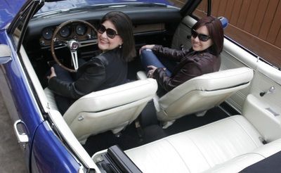 Two women are sitting in a blue convertible car