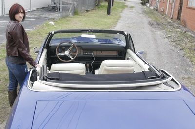 A woman is standing next to a blue convertible car