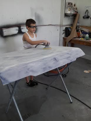 A young boy is sanding a piece of wood in a garage