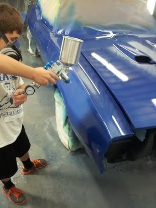A young boy is painting a blue car in a garage