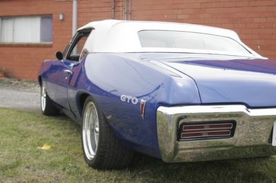 A blue gto car is parked in front of a brick building