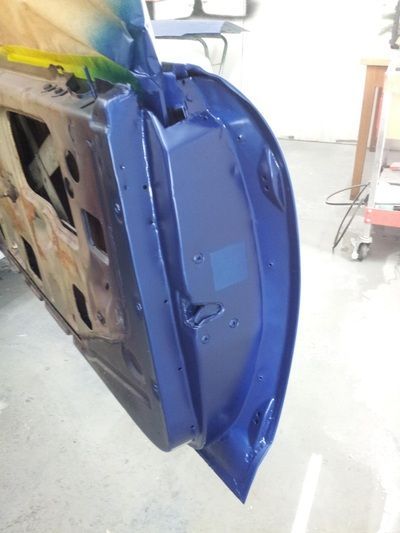 A blue car door is being painted in a garage