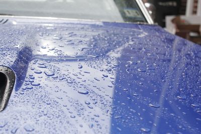 The hood of a blue car with water drops on it