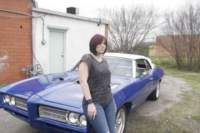 A woman is standing next to a blue car in front of a building