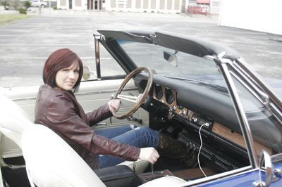 A woman is sitting in the driver 's seat of a blue convertible car