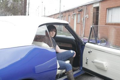 A woman is sitting in a blue car with the door open