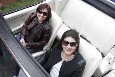 Two women are sitting in the back seat of a convertible car