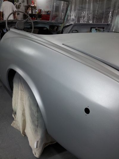 A silver car is being painted in a garage