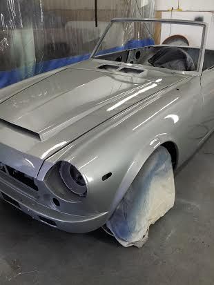 A silver car is sitting in a garage covered in plastic