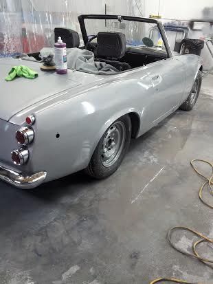 A silver convertible car is sitting in a garage being painted