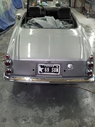 A silver convertible car with a texas license plate is parked in a garage