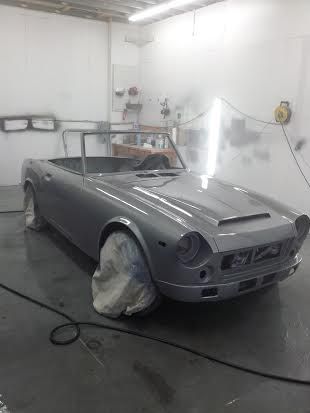 A silver sports car is being painted in a garage