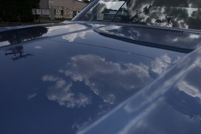 A close up of the hood of a blue car with clouds reflected in it