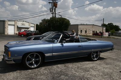 A blue convertible car is parked in a parking lot in front of a building