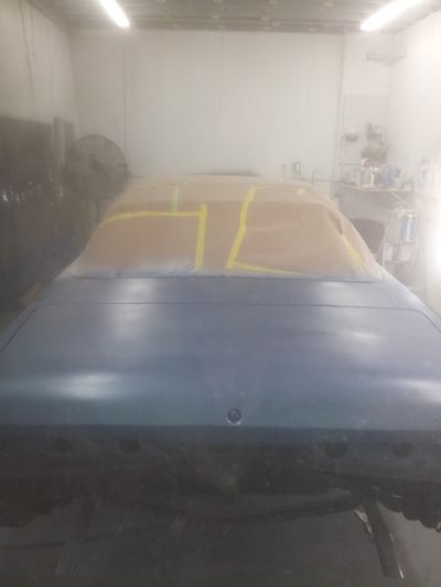 A blue car is being painted in a garage