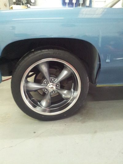 A blue truck with chrome wheels and tires is parked in a garage