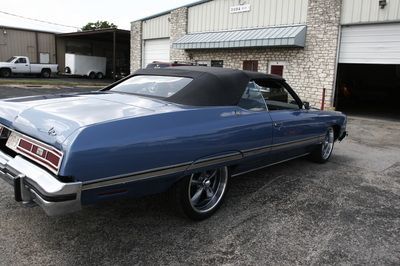 A blue car with a black top is parked in front of a garage