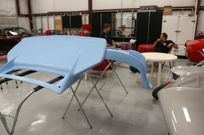 A man is sitting at a table in a garage with a car in the background