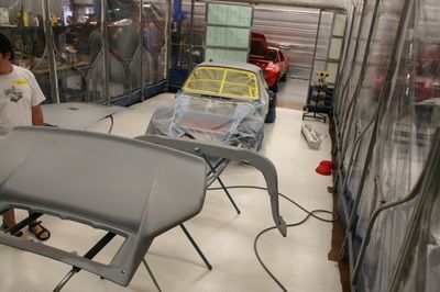 A man is standing in a garage next to a car that is being painted