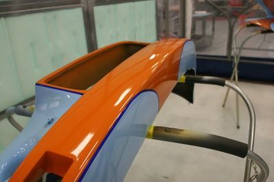 An orange and blue car is being painted in a garage