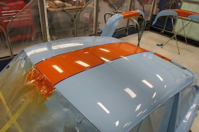 A blue and orange car is being painted in a garage