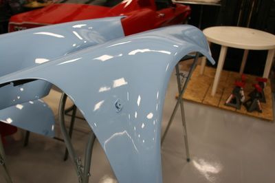 Two blue fenders are sitting on a table next to a red car