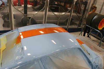A blue and orange car is being painted in a garage