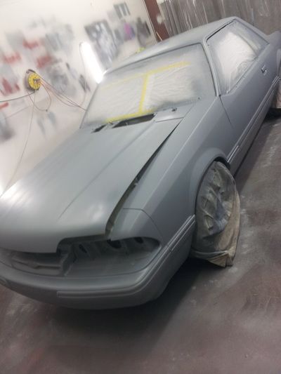A grey car is being painted in a garage