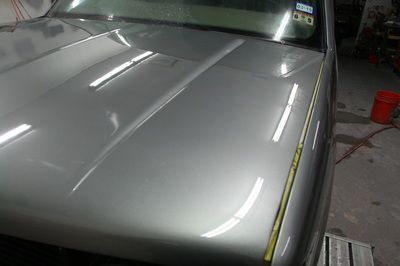 The hood of a silver car is being painted in a garage
