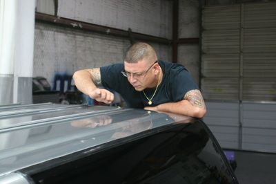 A man is working on the roof of a car in a garage