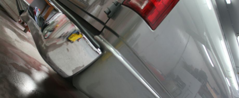 A silver car with a red tail light is parked in a parking lot