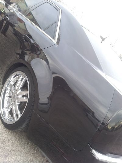 A black car with chrome wheels is parked on the side of the road