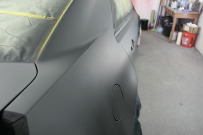 A black car is being painted in a garage