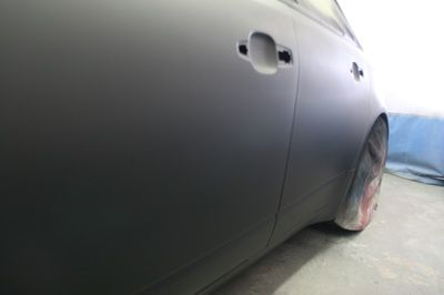 A black car is sitting in a garage being painted