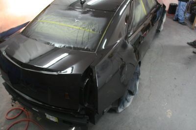 A black car is being painted in a garage