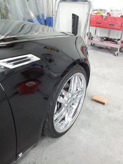 A black car with chrome wheels is parked in a garage