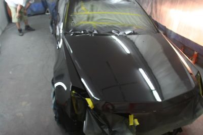 A black car is being painted in a garage