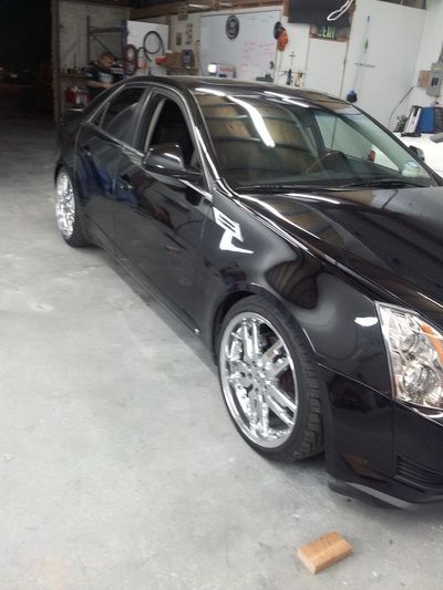 A black car with chrome wheels is parked in a garage