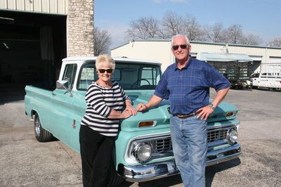 A man and a woman are standing next to a blue truck