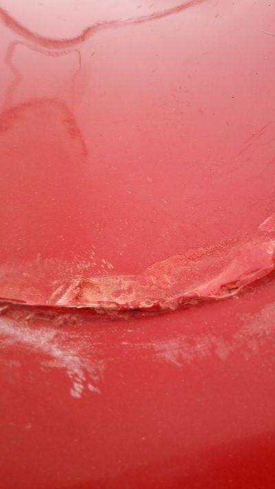 A close up of a red car with a damaged hood